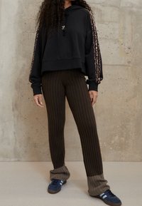 Felpa nera corta con strisce leopardate e cordino. Pantaloni marroni a coste con un design bicolore e orli a coste. Sneakers blu in suede.