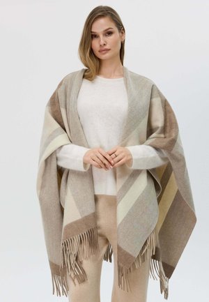 Sciarpa a strisce beige e marroni con dettagli frangiati, indossata sopra un maglione chiaro e abbinata a pantaloni beige, che mette in evidenza un tessuto morbido e strutturato.