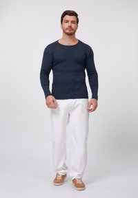 Navy ribbed knit long-sleeve shirt, paired with white pants and tan sneakers, featuring a round neckline and fitted silhouette.