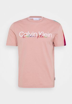 Jasnoróżowy t-shirt z krótkim rękawem z białym logo "Calvin Klein" i wielokolorowym napisem na piersi oraz tęczowymi paskami na rękawach.