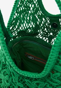 Vihreä virkattu kassi avonaisella ylhäällä, teksturoitu kangas ja sisäinen vetoketjullinen tasku, jossa on ruskea nahka-akseli.