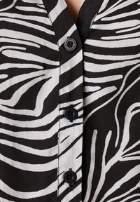 Black and white zebra-striped blouse with a buttoned front, featuring four black buttons and a soft, lightweight fabric texture.