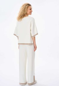 Witte gebreide outfit met een losvallend top en wijde mouwen, gecombineerd met bijpassende wijde broekspijpen. Afgewerkt met een beige accent aan de randen.