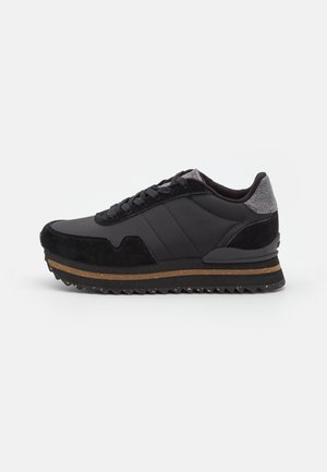 Zwarte lage sneaker met suède en stoffen panelen, grijze hielstrook, bruine streep op dikke zool en zwarte, getande rubberen buitenzool.