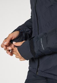 Námornícky modrá zateplená bunda s prešívaným dizajnom, elastickými manžetami so suchým zipsom a označením "OMNI-HEAT" na rukáve.
