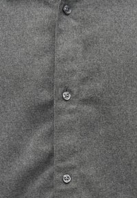 Chemise grise à boutons, fabriquée dans un tissu texturé, présentant une rangée de boutons sur le devant. Le tissu a un motif subtil et uniforme.