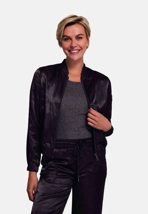 Black satin bomber jacket with a zip closure, round collar, and elastic cuffs. Paired with a grey fitted textured top and matching pants.