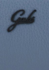 Logo "Gabs" in corsivo nero su una superficie di pelle blu chiaro testurizzata, centrato in primo piano.