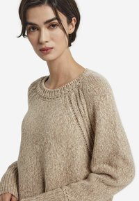 Beżowy sweter dzianinowy z teksturowanej włóczki, z prążkowanym dekoltem i mankietami, o luźnym kroju oraz subtelnymi diagonalnymi przeszyciami.