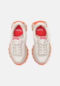 Białe i beżowe sneakersy z pomarańczowymi gumowymi podeszwami, okrągłym czubkiem i sznurowadłami. Posiadają czerwoną metkę z logo na języku i wyściełane wnętrze.