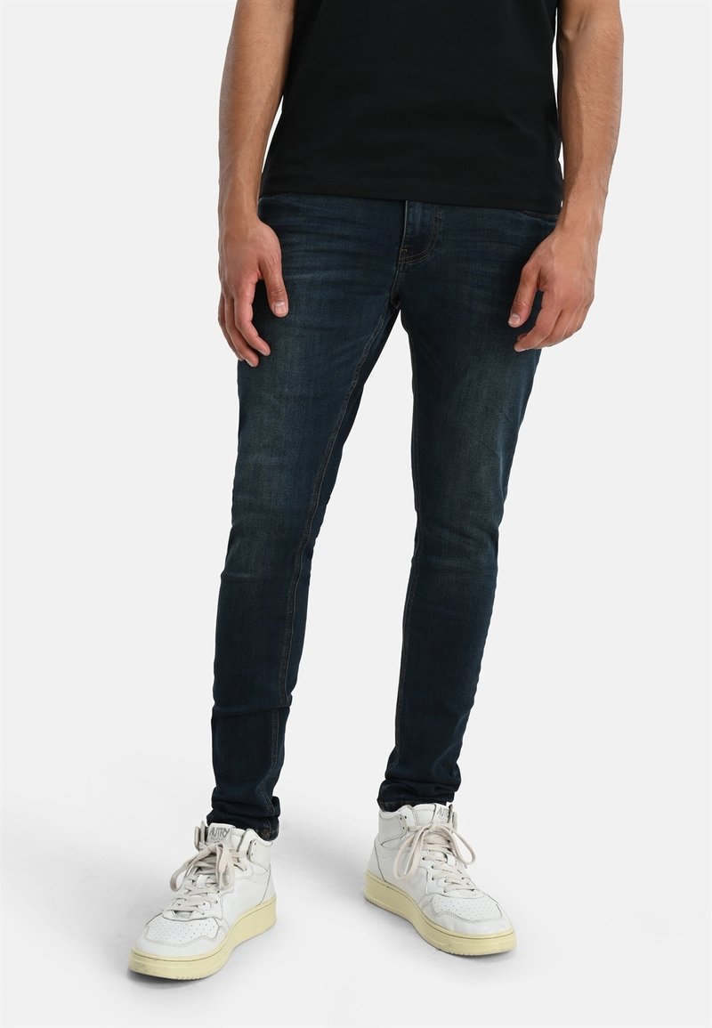Mörkblå denimjeans med slim fit, featuring en medelhög midja och minimal blekning. Kommer med vita högtoppsskor.