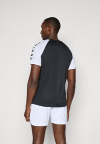 T-shirt de sport à manches courtes noir et blanc avec un dos noir et un devant blanc, arborant le mot "FEARLESS" sur l'épaule.