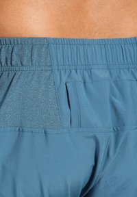 Pantalones cortos deportivos azules con una cinturilla elástica, textura suave y un bolsillo trasero con un patrón sutil.