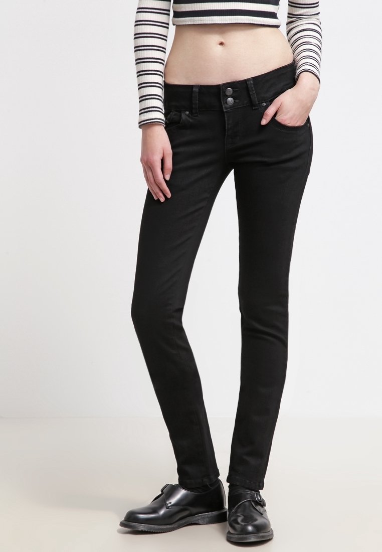Jeans negros ajustados con un diseño ceñido, textura suave y costuras sutiles, combinados con zapatos negros y una camiseta de manga larga a rayas.