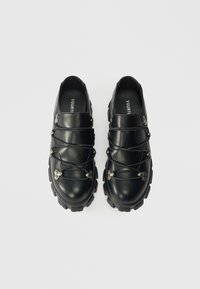 Fekete bőr cipők lekerekített orral, kiemelkedő fűzős megoldással, fémes kiegészítőkkel és mintázott gumitalppal a tapadás és a támogatás érdekében.