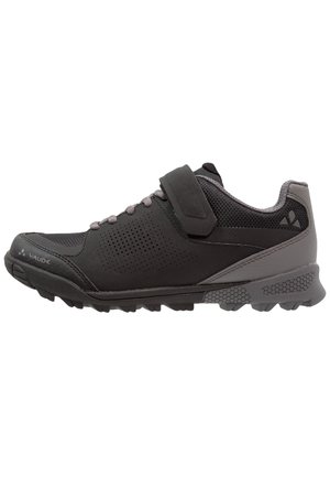 Chaussure de sport noire et grise avec lacets et bande Velcro, côtés perforés, semelle texturée, et logos de la marque sur les zones des orteils et du talon.