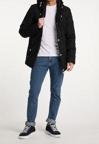 Giacca nera isolante con cappuccio, bottoni a pressione, chiusura con zip e due tasche frontali. Abbinata a jeans blu e sneakers blu navy.