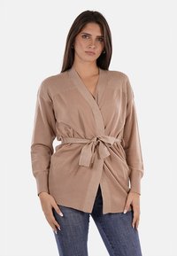 Cardigan beige lavorato a maglia con una cintura in vita, texture a coste sulle maniche e sulle spalle, apertura frontale e maniche lunghe. Design casual.