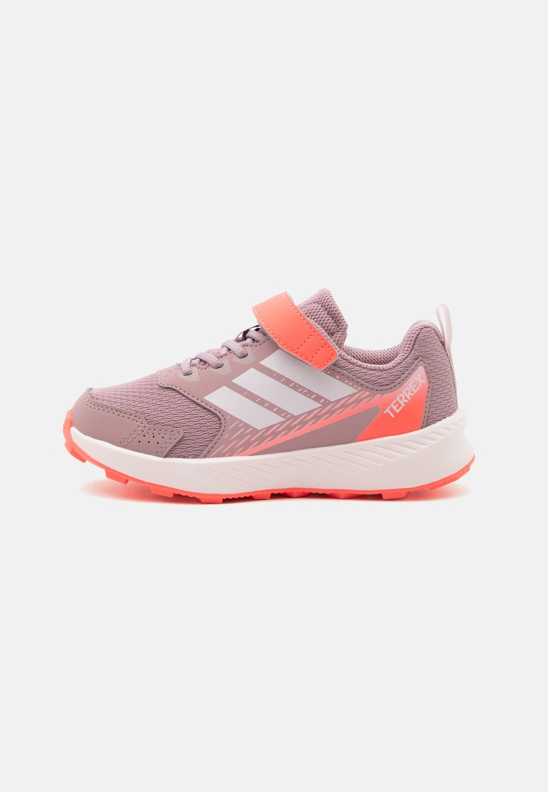 Παιδικό ροζ και κοραλλί αθλητικό παπούτσι Adidas Terrex με λευκές ρίγες, ιμάντα με βέλκρο και υφή στην σόλα, στραμμένο προς τα αριστερά σε λευκό φόντο.