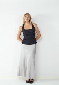 Top nero a fascia con tessuto testurizzato e scollo quadrato, abbinato a una lunga gonna maxi grigia in satin fluente. Scarpe nere completano l'outfit.