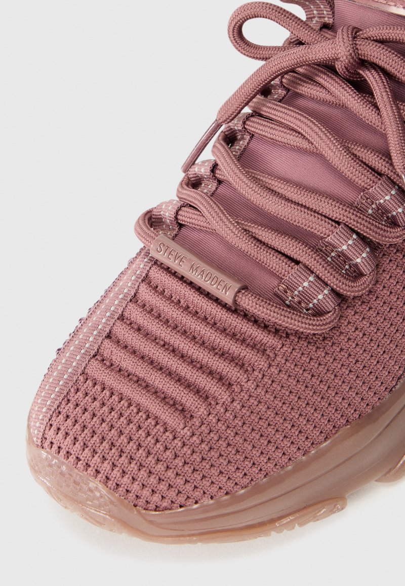 Gros plan sur une basket mauve avec un tissu texturé, des lacets épais et une étiquette logo "Steve Madden" sur le côté. Semelle en caoutchouc transparent visible.