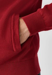 Red knit sweater featuring a side pocket, ribbed cuffs, and textured fabric, highlighting its warm, casual design.