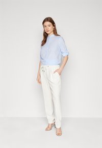Camicia button-up azzurro chiaro con maniche arrotolate, abbinata a pantaloni bianchi larghi con vita regolabile e una leggera lucentezza.