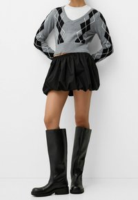 Grå stickad tröja med svart argyle-mönster, svart ballongsarkjol och knähöga svarta läderstövlar med rund tå och låg sula.