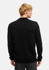 Zwarte gebreide trui met lange mouwen, een ronde hals en ribgebreide manchetten en onderkant. Glad textuur zonder zichtbare patronen of details.