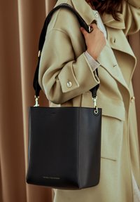 Zwarte leren tote bag met gouden hardware, met een gestructureerde vorm en korte handvatten. Geaccentueerd met "Victoria Hyde London" aan de onderkant.