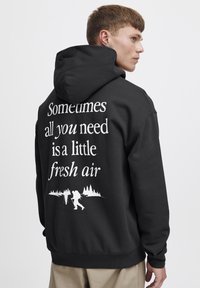 Sudadera negra con un gráfico en la parte posterior que muestra texto en blanco y una ilustración de excursionistas contra una silueta de bosque.