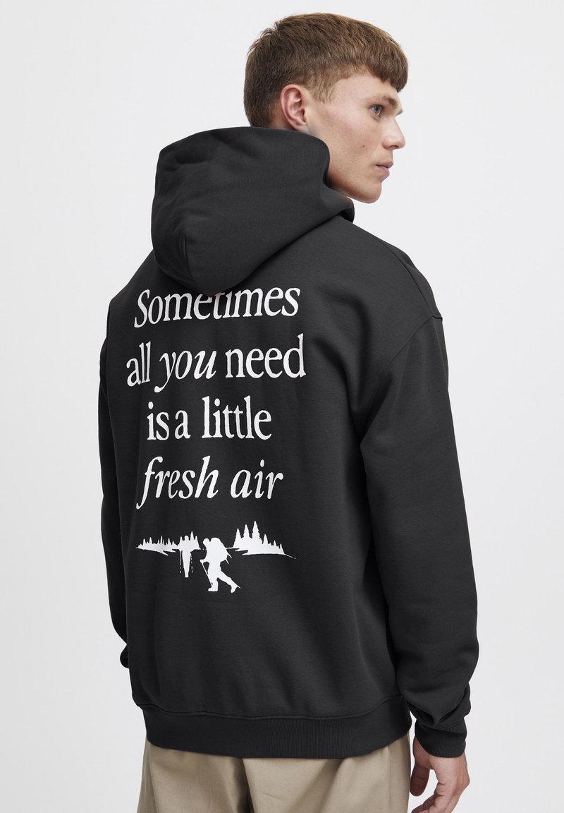 Sudadera negra con un gráfico en la parte posterior que muestra texto en blanco y una ilustración de excursionistas contra una silueta de bosque.