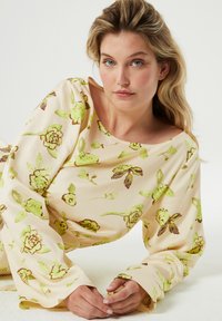 Crème blouse met een bloemenpatroon in groen en bruin. Beschikt over brede mouwen en een bateau-halslijn. Zachte textuur en een relaxte pasvorm.