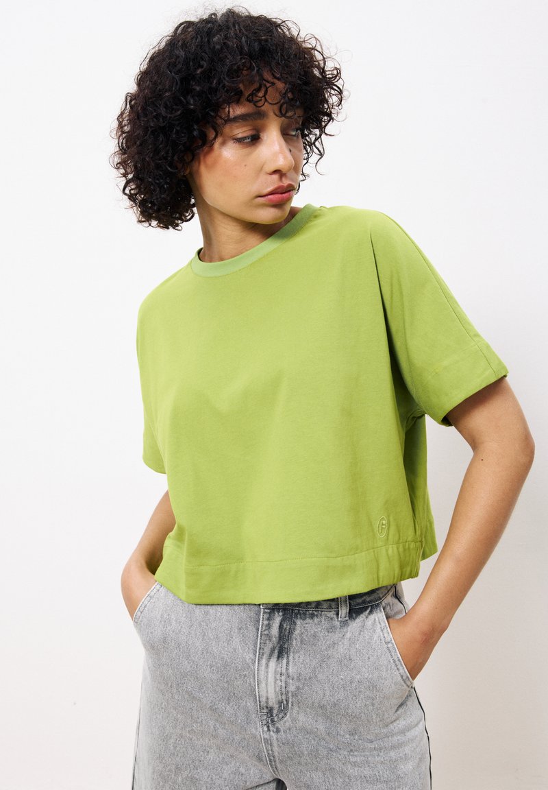 T-shirt en coton vert lime à manches courtes avec un col rond, design court et un subtil logo au niveau de l'ourlet. Assorti avec un pantalon gris.