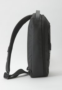 Zaino in tessuto nero con forma rettangolare, tracolla regolabile e testurizzata, maniglia superiore e chiusura con zip. Presenta il logo sul lato.