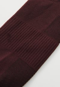 Calcetín burdeos de punto que presenta secciones texturizadas y lisas, con un diseño estampado y una textura acanalada en varios estilos de tejido.