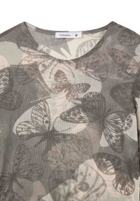 Top lungo trasparente grigio con stampa di farfalle in varie tonalità. Collo rotondo, leggermente lucido e etichetta del marchio visibile.