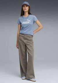 Light blue cotton t-shirt with white "PUMA" logo, paired with light grey wide-leg trousers and blue sneakers. Accessories include a matching cap.