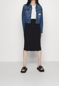 Denimjacka, blå, kort design med knappar, över vit t-shirt. Svart tajt kjol, slät textur. Svarta sandaler med breda remmar.