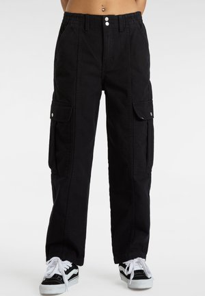 Schwarze Cargo-Hose mit elastischem Bund, Klappentaschen an den Seiten, getragen mit schwarz-weißen Turnschuhen und freiem Bauch mit Bauchnabelpiercing.