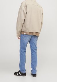 Béžová džínová bunda, hnědá košile pod ní, světle modré džíny, černé tenisky s bílými pruhy, viděné zezadu. Jednoduchý, ležérní design.