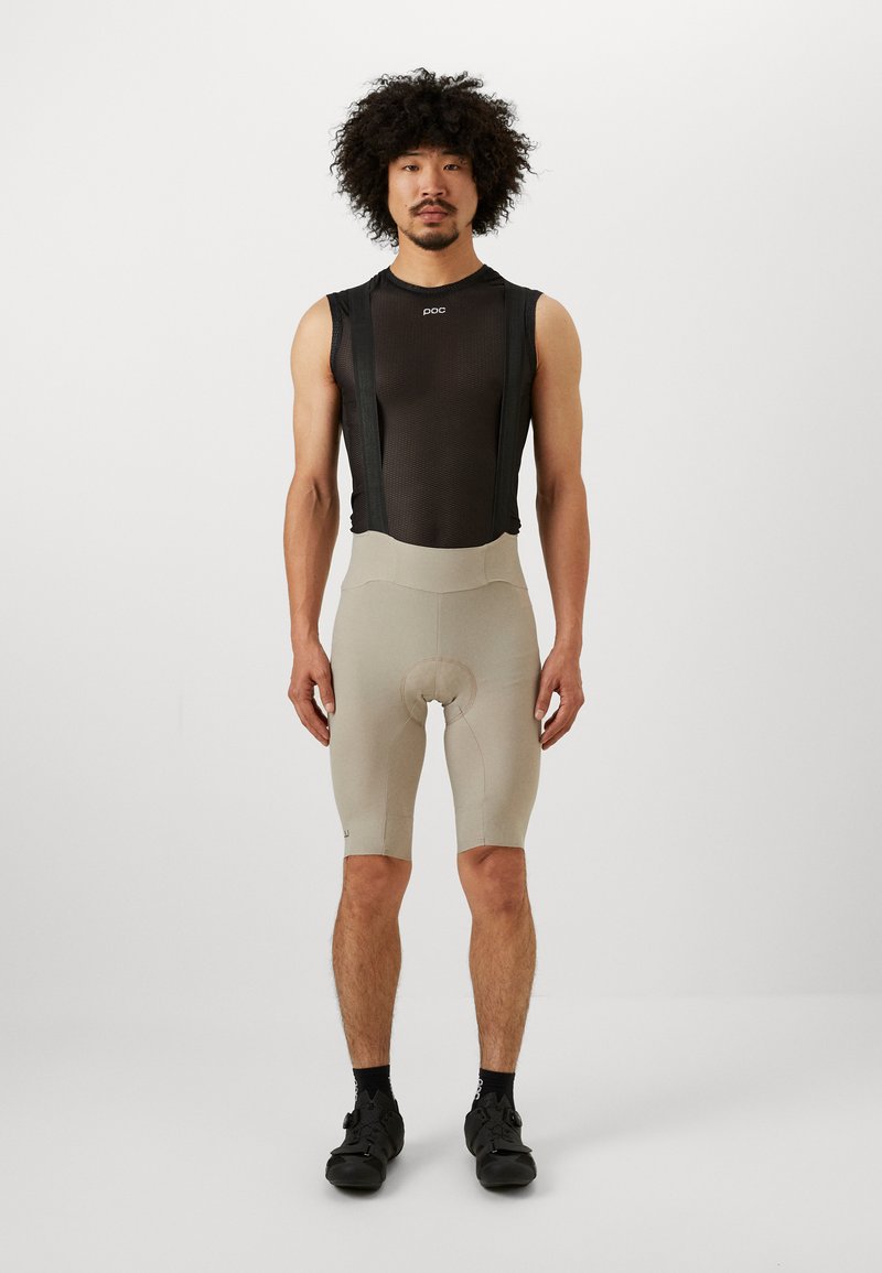 Fahrrad-Outfit mit einem schwarzen, ärmellosen Mesh-Trikot und beige Shorts. Die Shorts haben ein gepolstertes Einsätze und sitzen körpernah.
