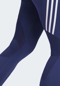 Námořnické modré sportovní legíny s hladkou texturou, s bílými třemi pruhy na straně a síťovými panely pro prodyšnost.