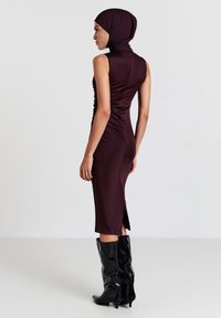 Abito aderente bordeaux con colletto alto, dettagli arricciati e spacco laterale. Abbinato a stivali neri alti e lucidi. Tessuto liscio con una finitura elegante.