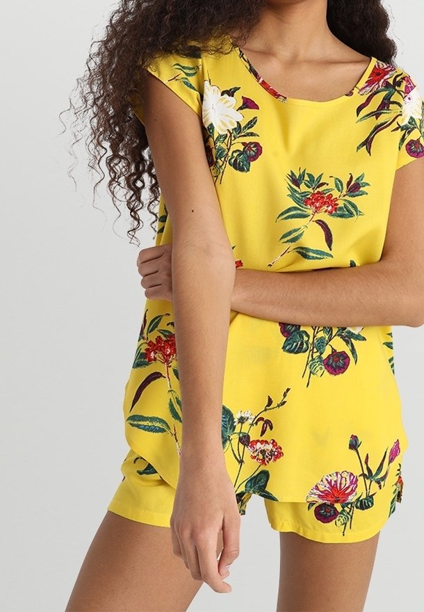 Tenue jaune à motifs floraux comprenant un haut à manches courtes et un short, avec une coupe ample et des fleurs multicolores vives sur le tissu.