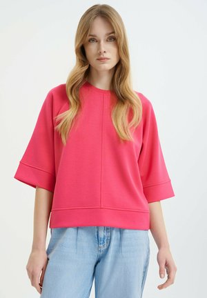 Roze sweatshirt met een ronde halslijn, driekwart mouwen en een relaxte pasvorm. Gemaakt van een zachte, textuurstof. Te combineren met lichtblauwe spijkerbroek.