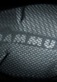 Svart tyg med en hexagonal mönster, med texten "MAMU" i en ljusare nyans som skapar kontrast i texturen.