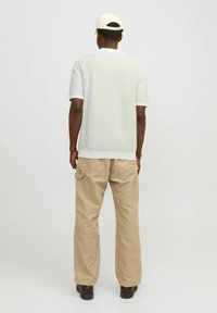 Bílá texturovaná polo košile s krátkým rukávem, spárovaná s béžovými cargo kalhotami s bočními kapsami. Model se otáčí zády, na hlavě má světlou kšiltovku.