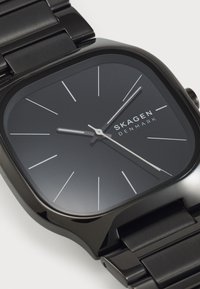 Orologio in acciaio inossidabile nero con quadrante quadrato, faccia minimalista grigia, indicatori delle ore argentati e bracciale elegante. Presenta un logo del marchio ben visibile.