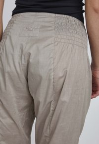 Light beige elastic waist pants with side pockets, featuring a textured, wrinkled fabric. Label stitched on the back. Casual design.